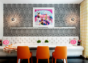 DHD Chelsea Townhouse Family Room - with 3 orange chairs, a bright pink and white art piece in the center, white custom banquette and black and white pattern wallpaper with two silver sconces on either side of art