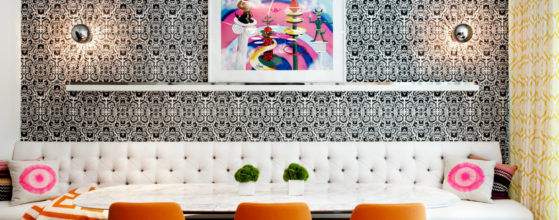 DHD Chelsea Townhouse Family Room - with 3 orange chairs, a bright pink and white art piece in the center, white custom banquette and black and white pattern wallpaper with two silver sconces on either side of art